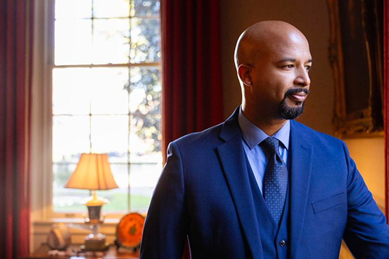 Un hombre está de pie en una vieja oficina, mirando a la derecha. Hay una ventana detrás de él.